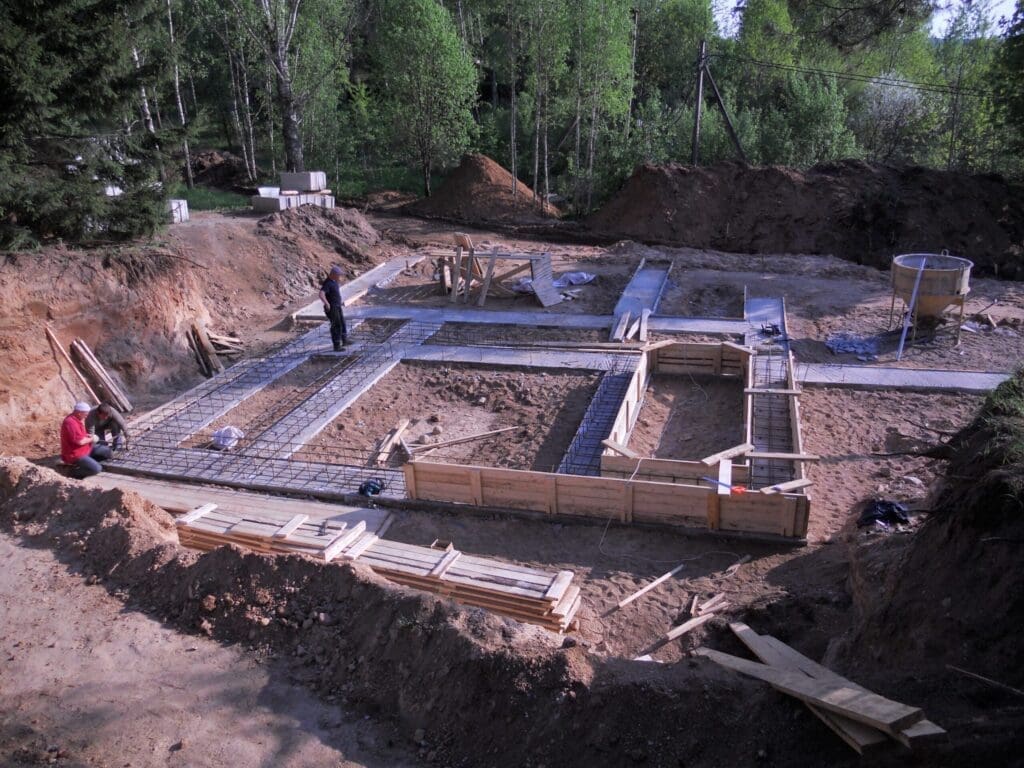 Two people working on a house foundation construction site in a wooded area.