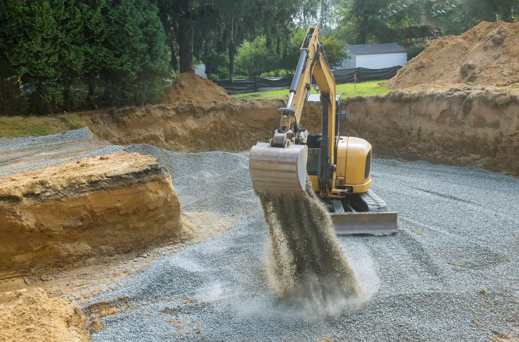 Yellow excavator digging and spreading gravel on a construction site.