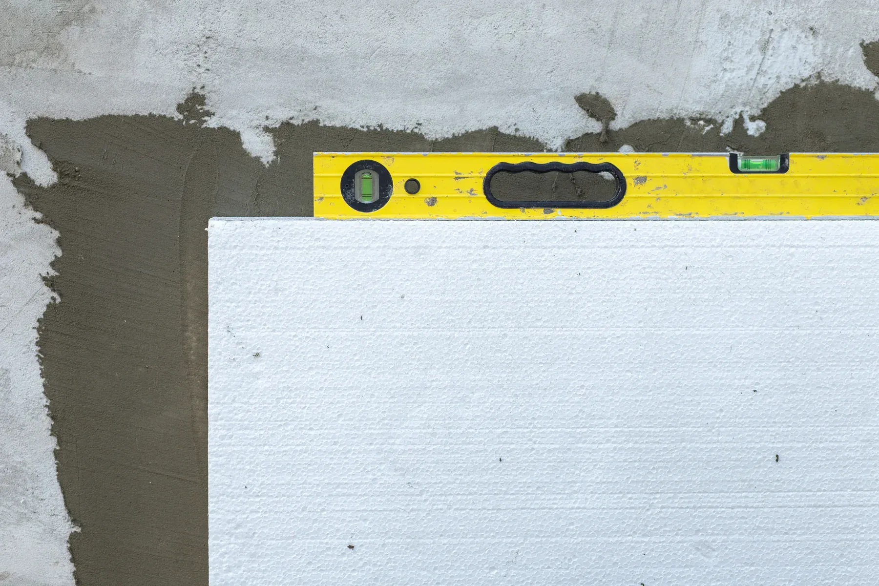Yellow spirit level on white insulation board against a concrete wall.