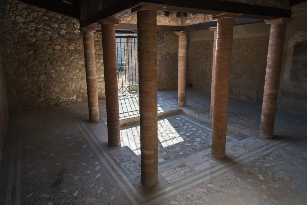 Ancient Roman room with brick columns, mosaic floor, and stone walls