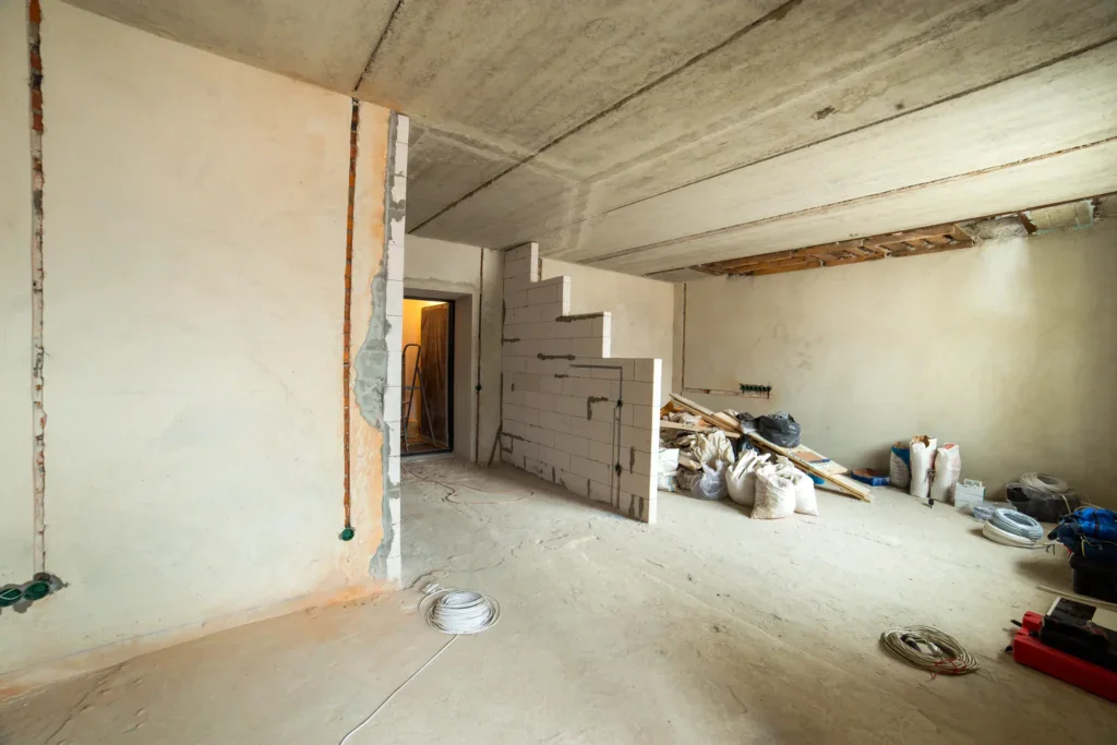 Unfinished room with concrete walls, floor, and ceiling, showing construction materials.