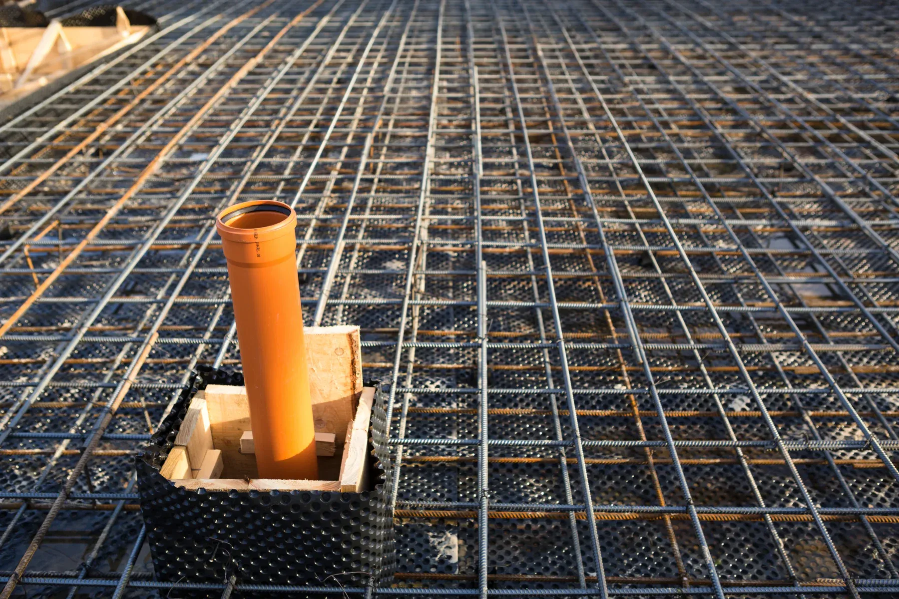 Orange pipe on a construction site with metal mesh reinforcement.