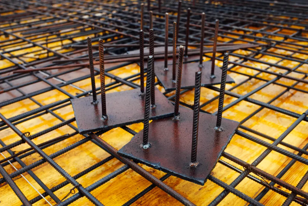 Close-up of rebar grid and metal plates with vertical rods on a construction site.