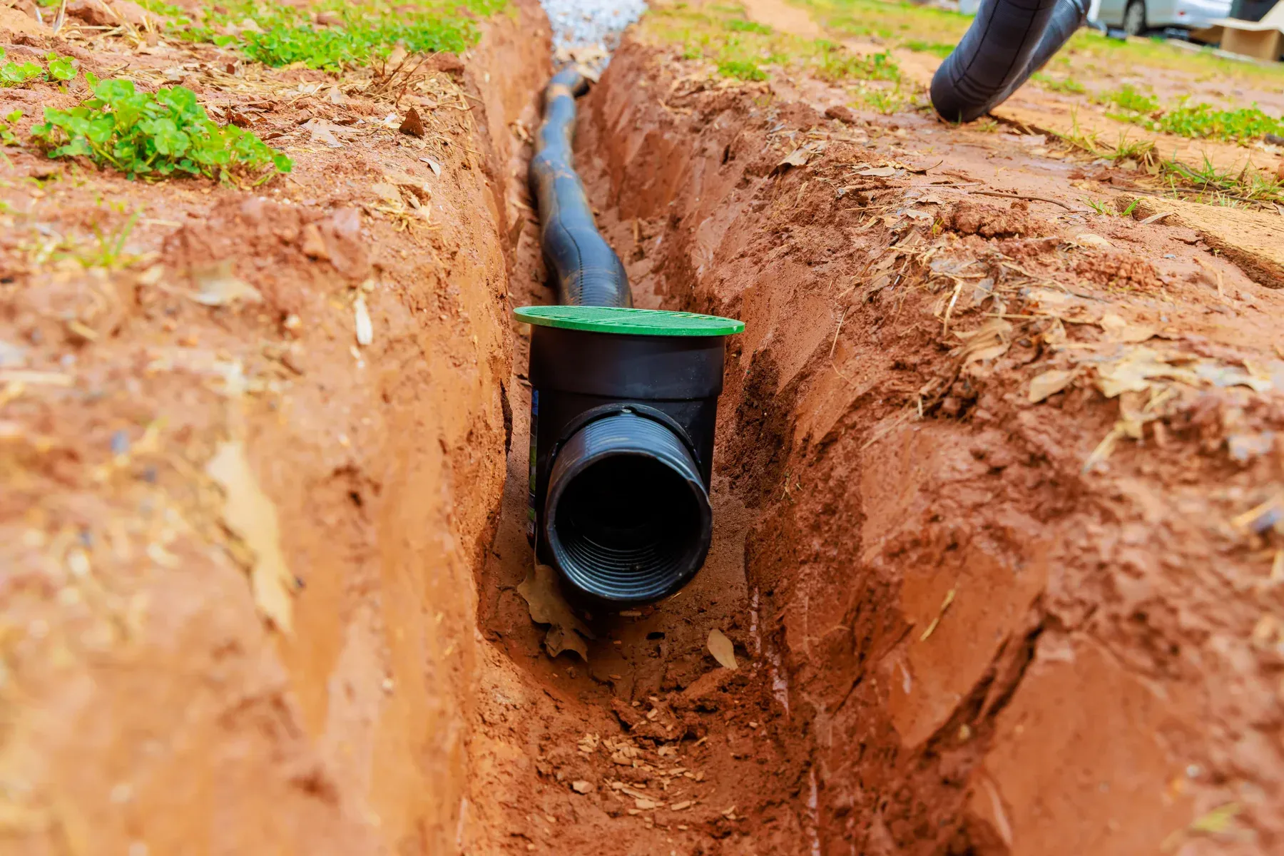Black drainage pipe with green cap in a trench of red dirt.