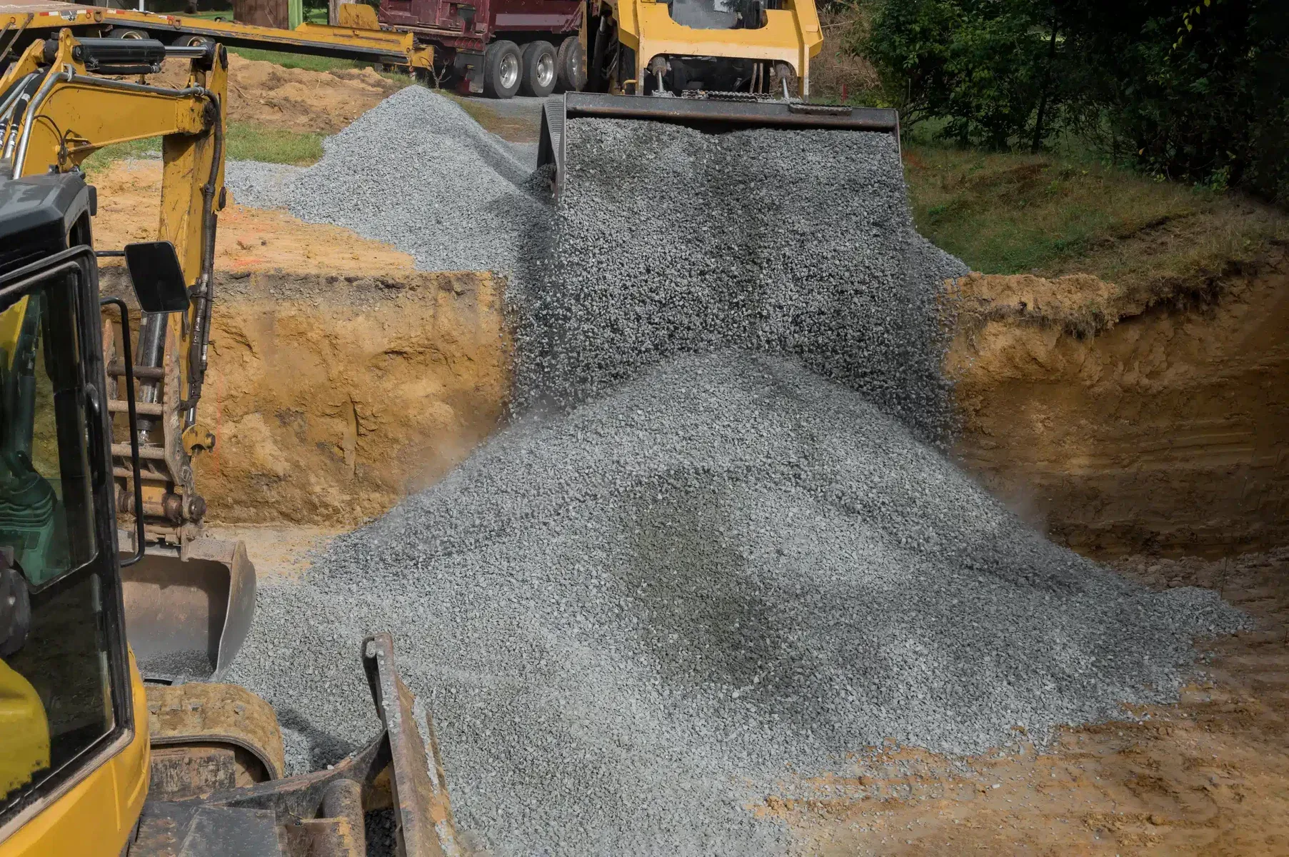 Heavy machinery dumping gravel into a large pile on a construction site.