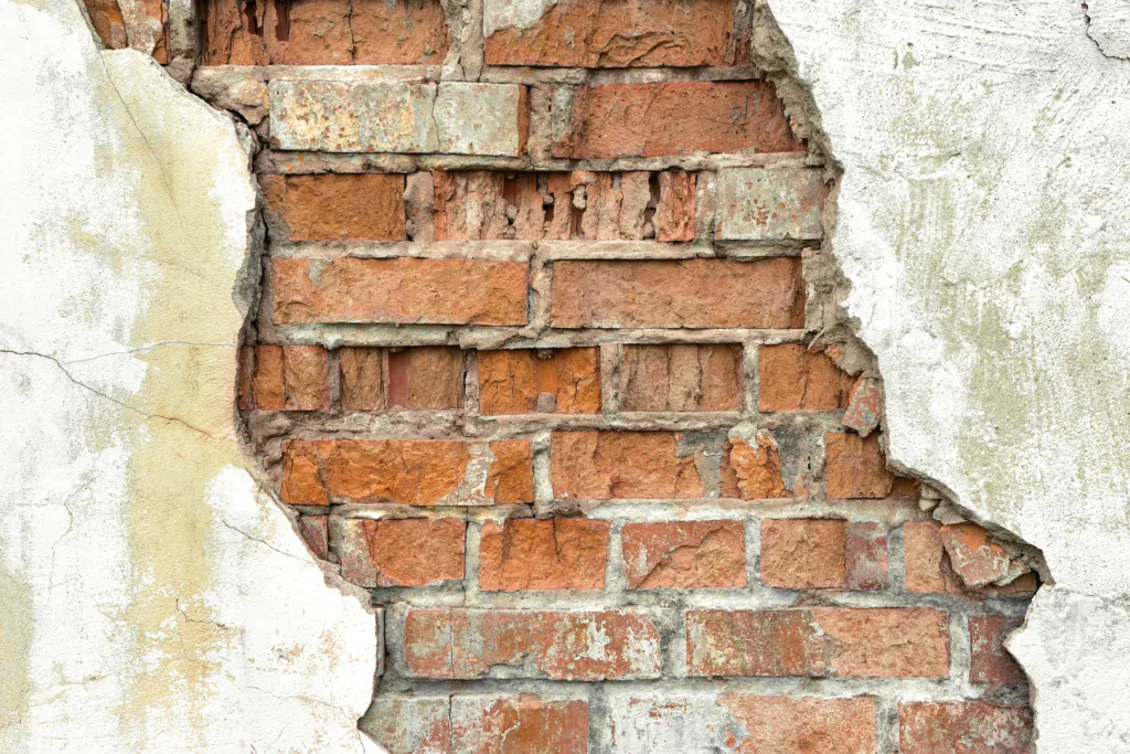 Close-up of a damaged brick wall with peeling white plaster