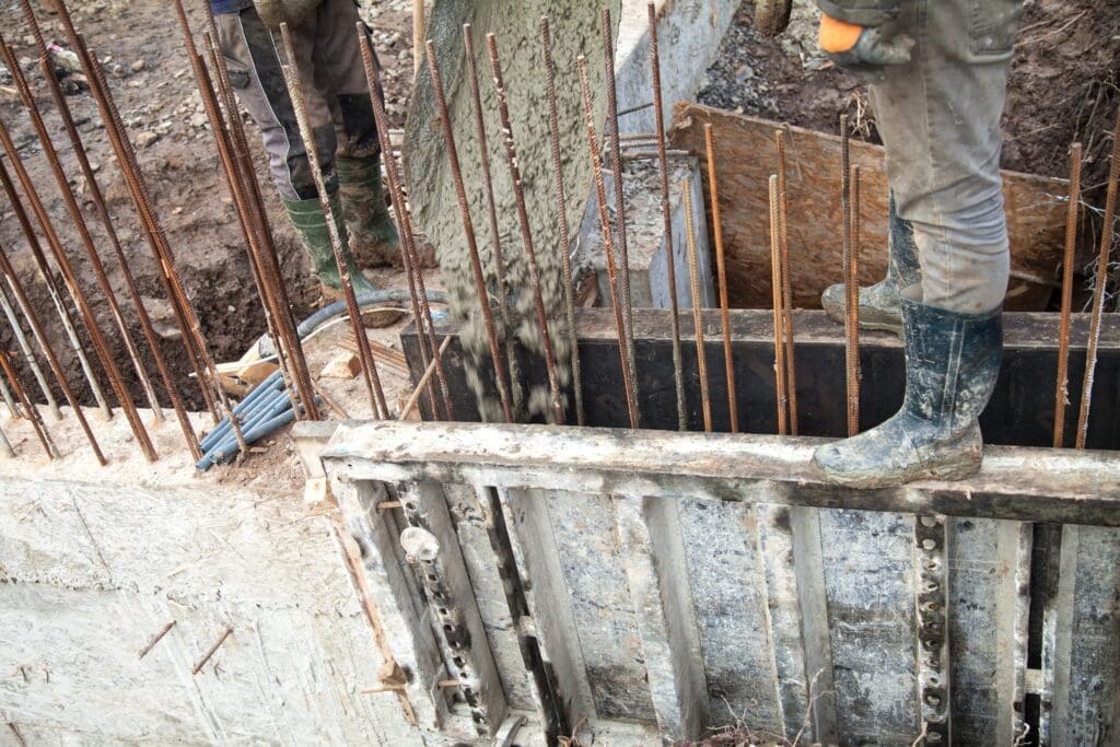 Construction workers pouring concrete into a foundation with rebar and wooden forms.