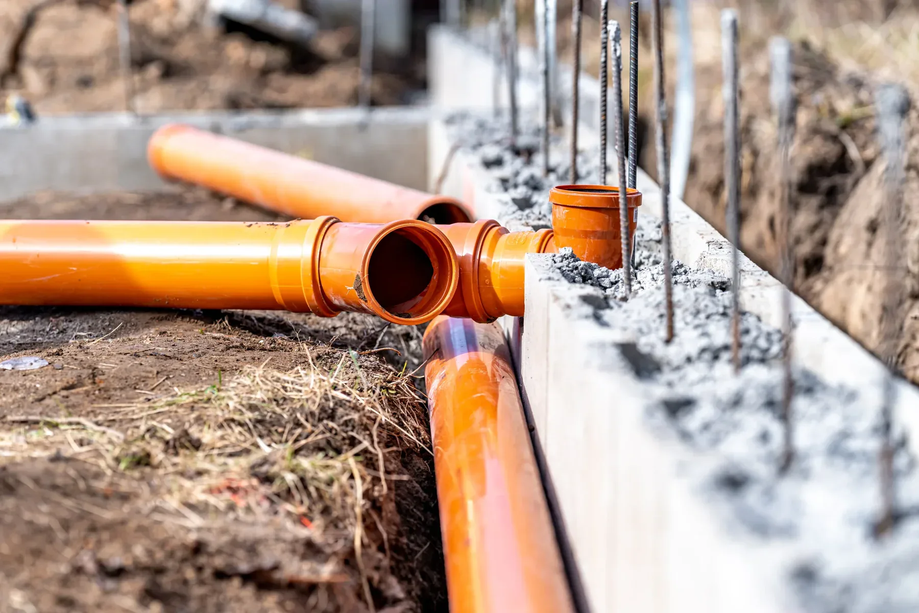Orange drainage pipes laid in a trench next to a concrete foundation.