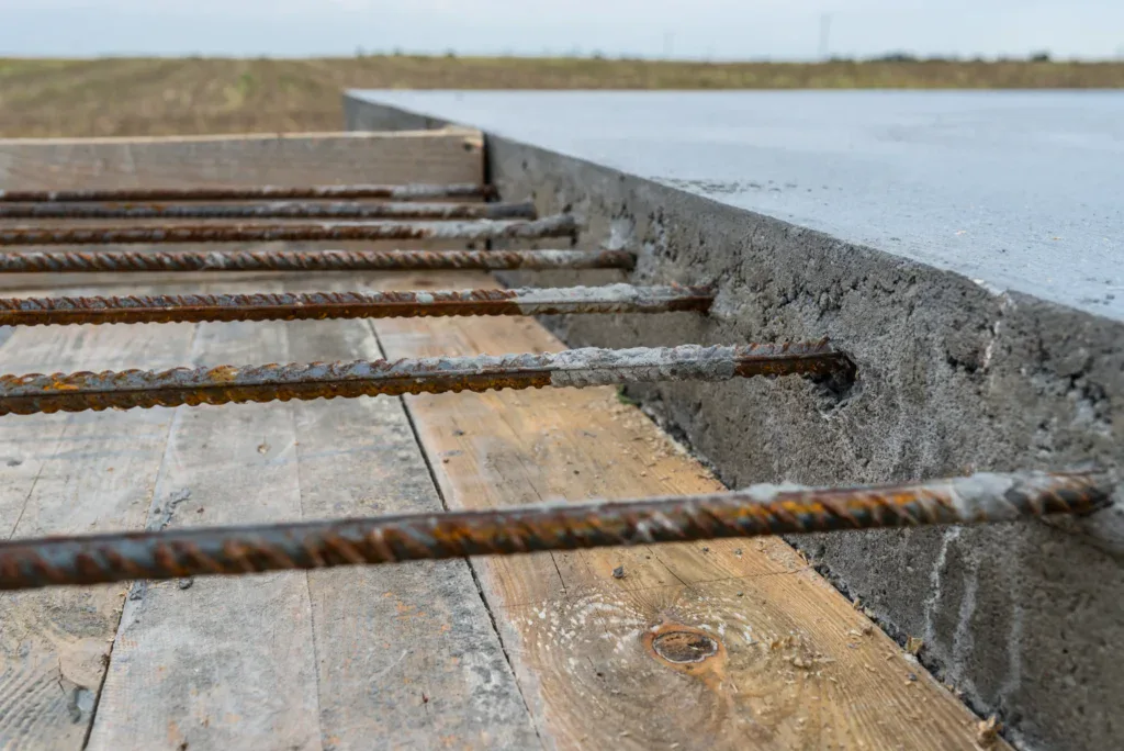 Close-up of rebar extending from a concrete slab on wooden forms.