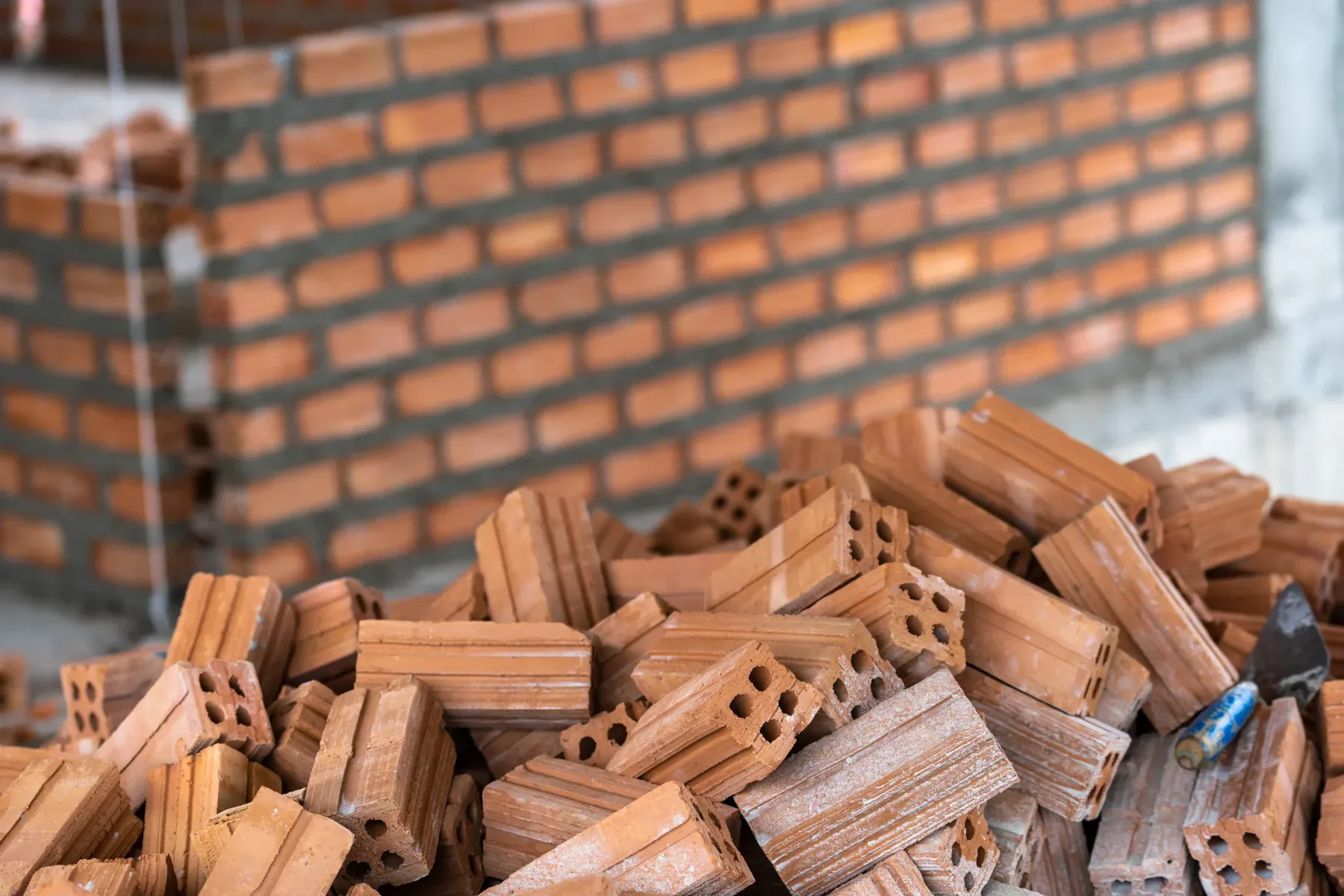 Pile of red bricks with a trowel, a brick wall in the background