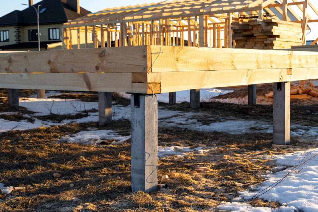 Raised wooden house foundation on concrete pillars in a snowy field