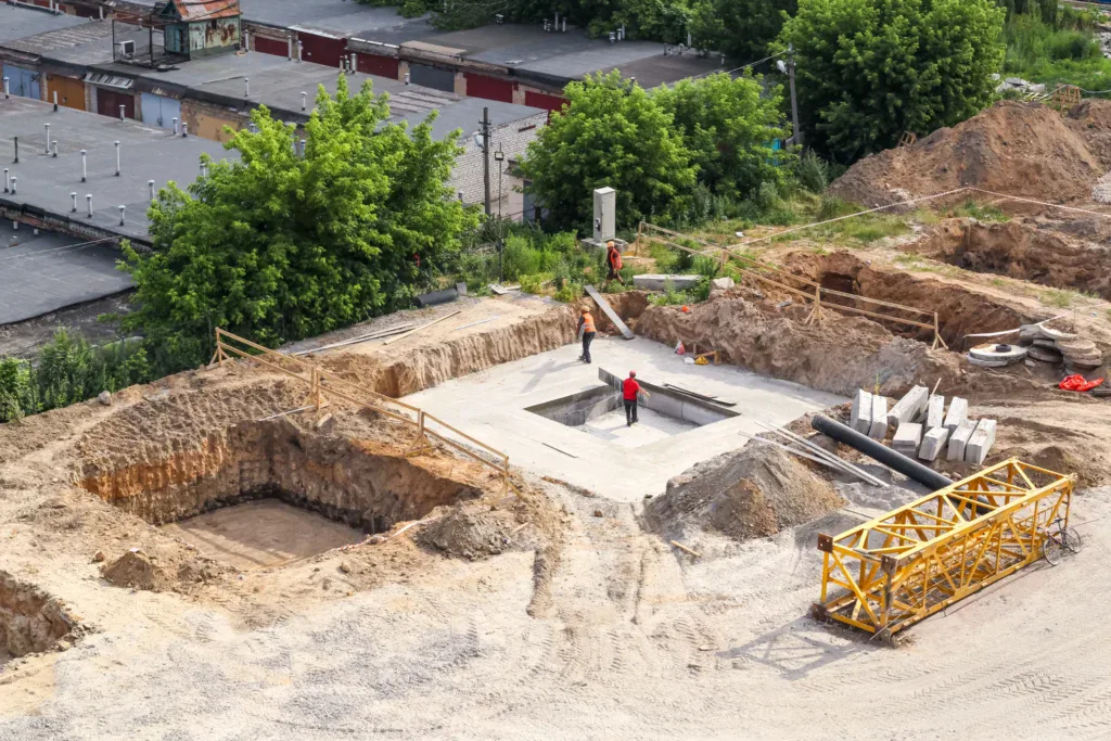 Construction site with workers, excavated pits, and a yellow crane.