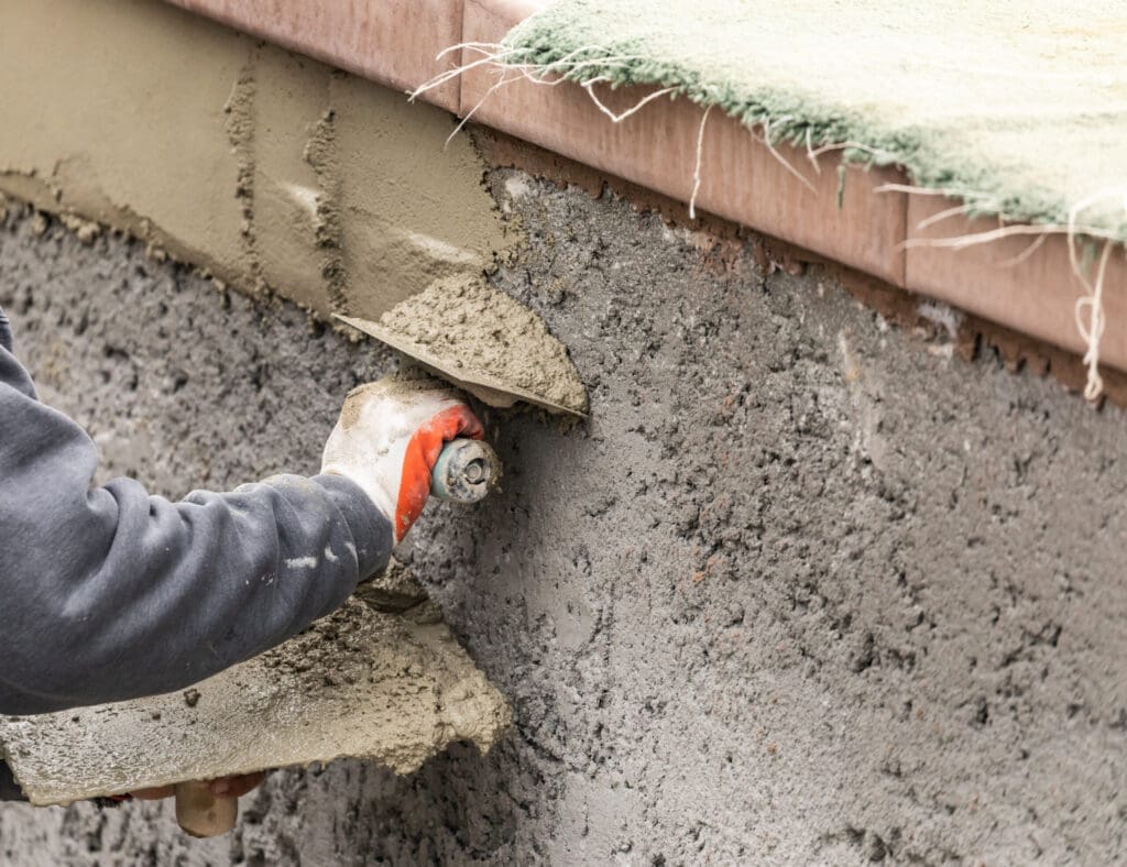 Person applying cement plaster to a wall with a trowel.
