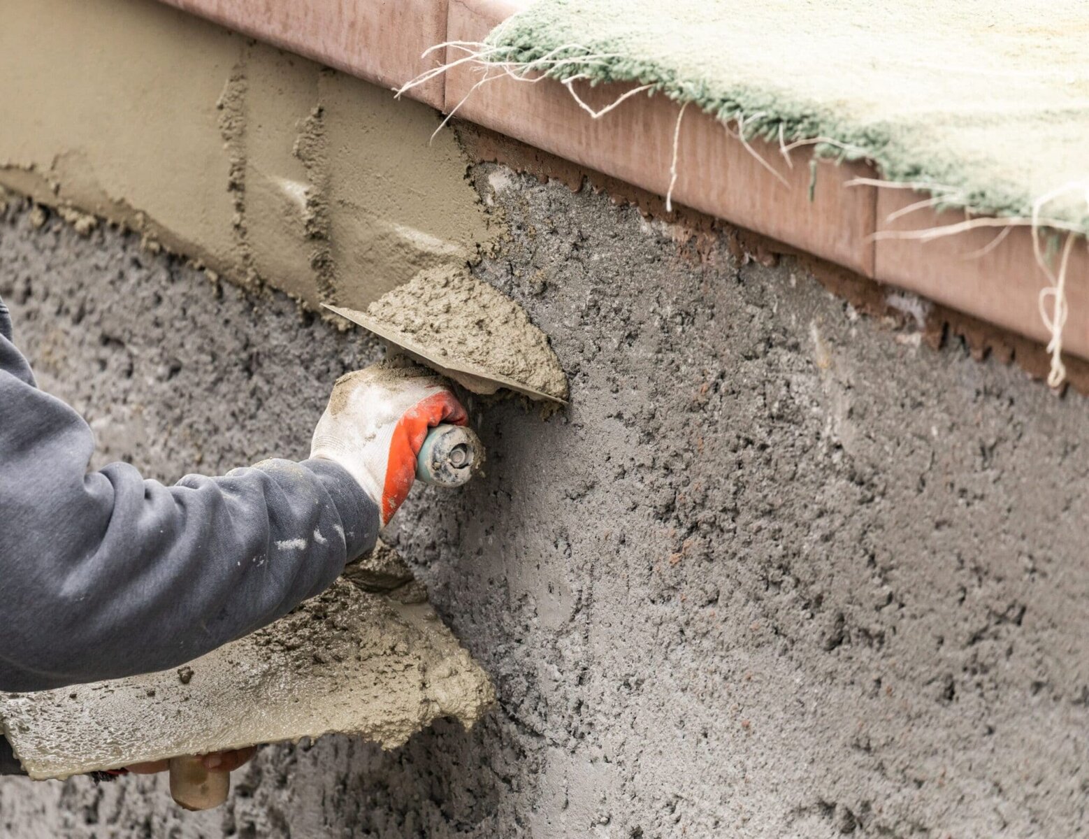Person applying cement plaster to a wall with a trowel.
