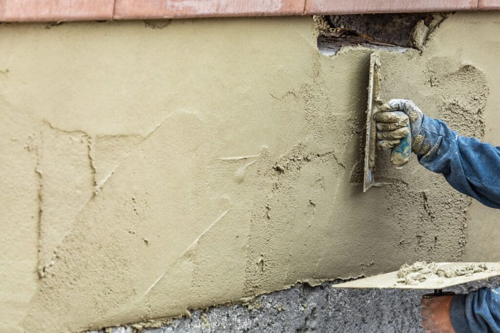 Person applying stucco to a wall with a trowel