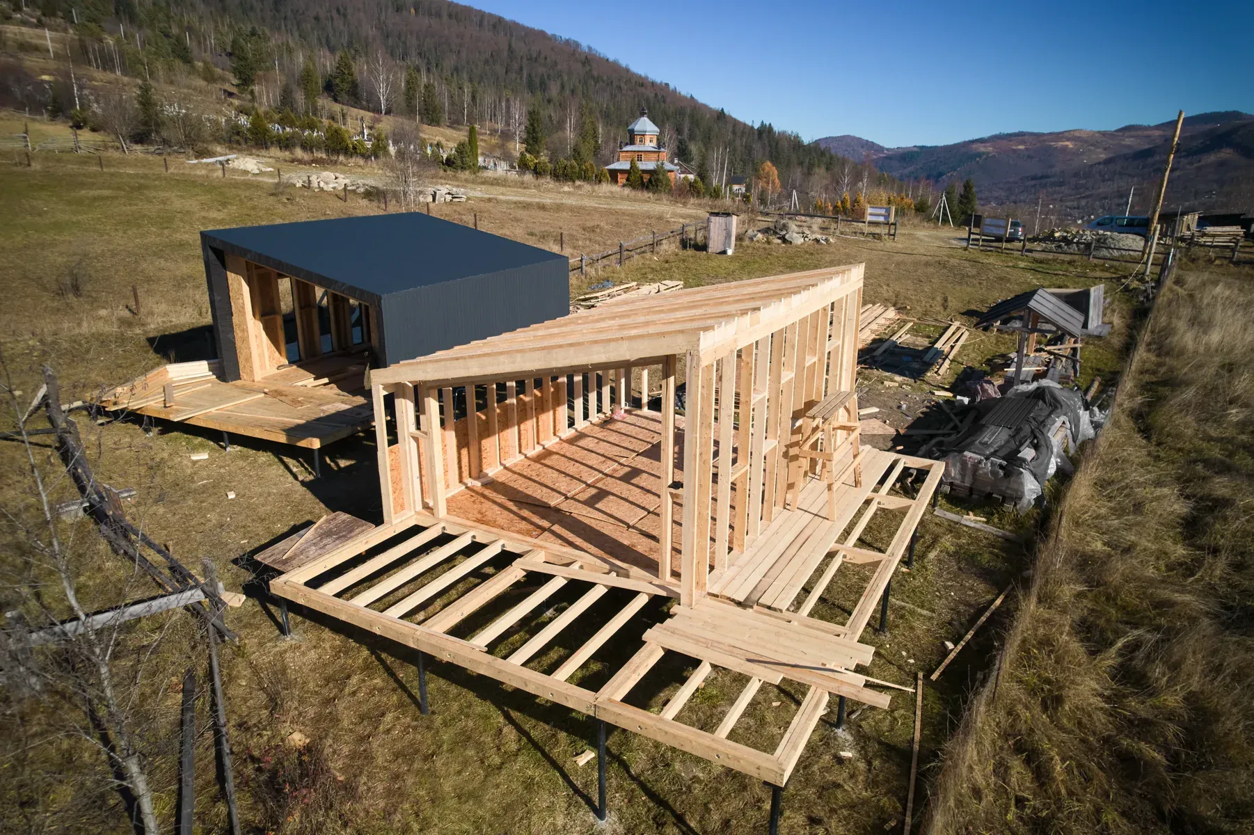 Two modern houses under construction in a rural, mountainous area.