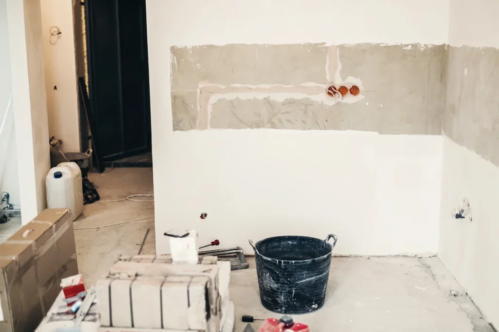 Room under renovation with exposed wiring, bucket, and construction materials.