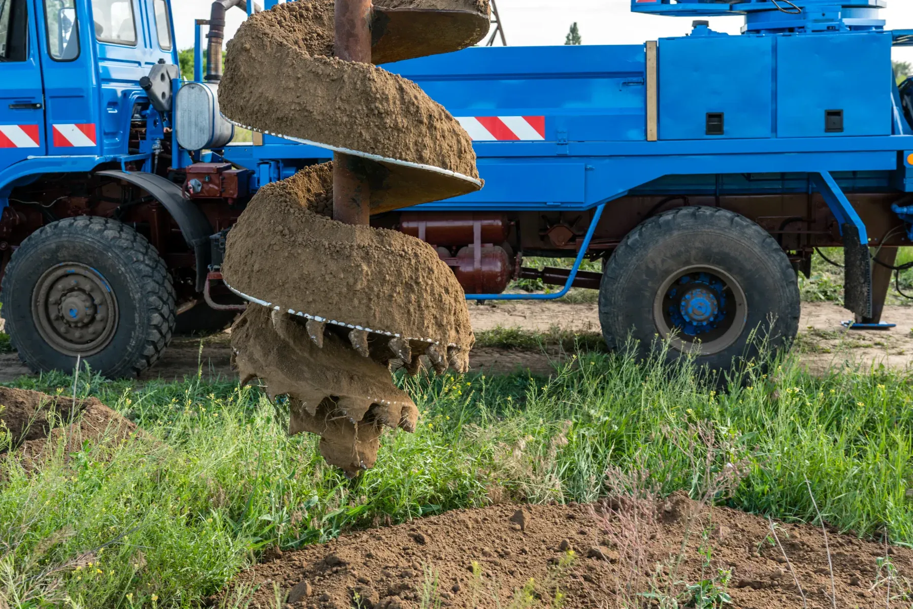 Large blue drilling truck with an auger in the ground