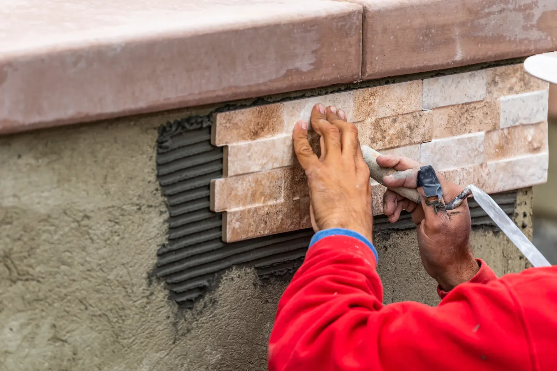 Person installing rectangular stone tiles on a wall with mortar.