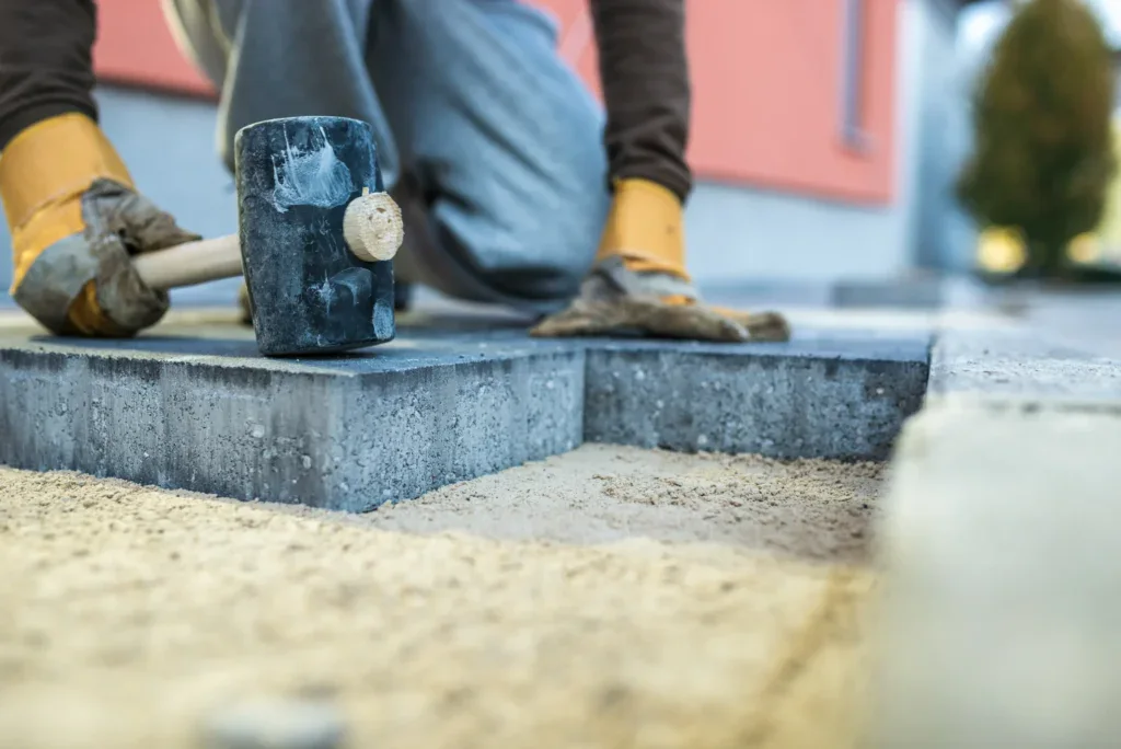 Person in work gloves using a rubber mallet to install paving stones.