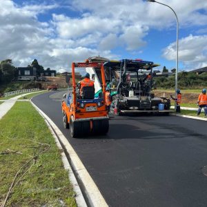 Asphalt paving work on a suburban street with construction workers and machinery.