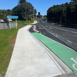 Wide sidewalk and dedicated bicycle lane on urban street with traffic signals and directional signage.
