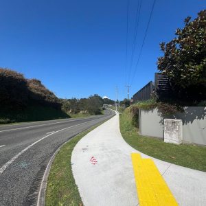 New Zealand sidewalk with tactile paving and road access, in a scenic suburban area.