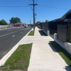 New Zealand residential sidewalk with modern fencing and clear blue sky.