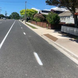 Bright suburban street scene in New Zealand with well-maintained homes and a clear blue sky.