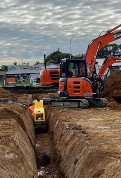 Excavator digging trench for plumbing and drainage installation on construction site.