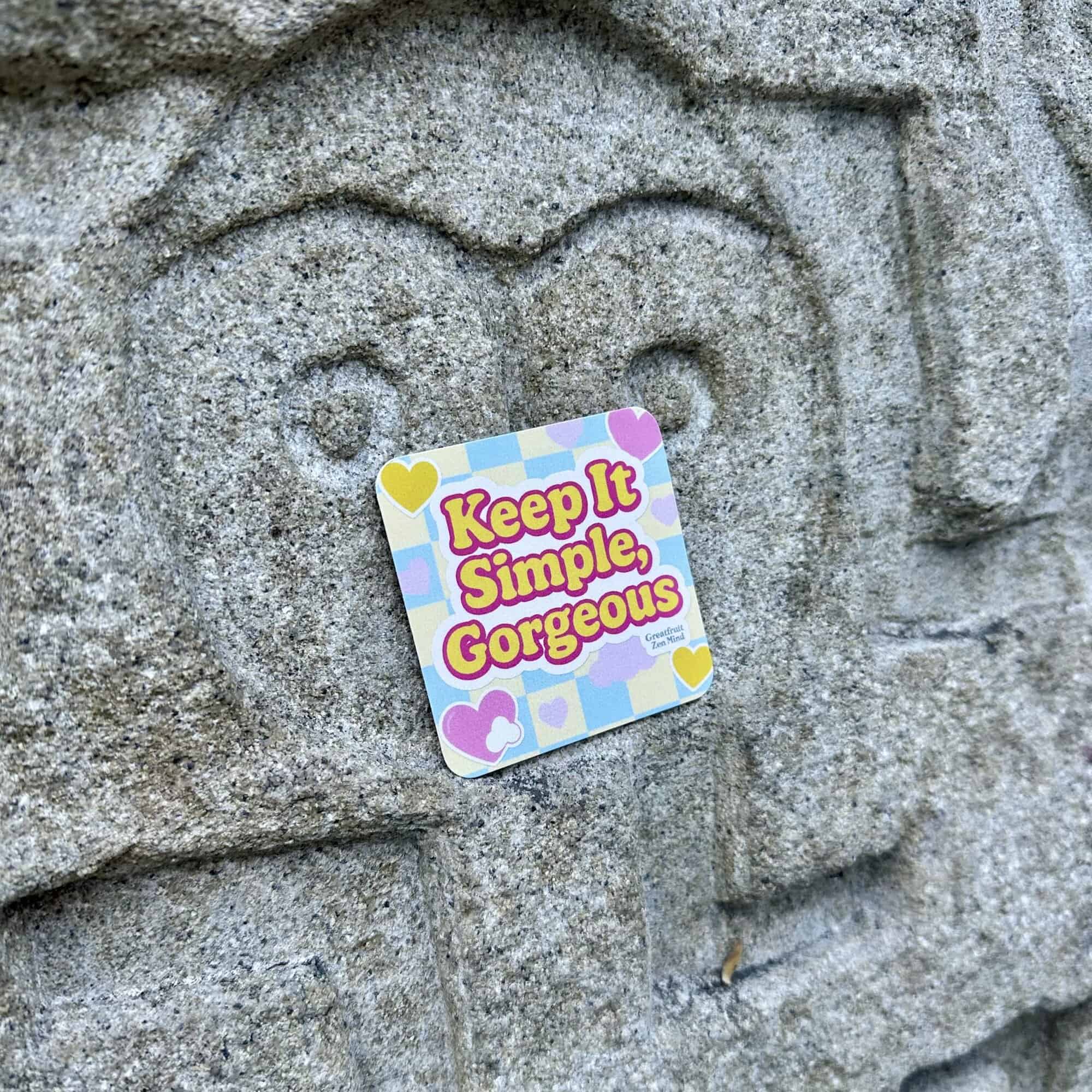 A Pocketful of Zen card resting upon a boulder with an owl's face carved into it. Text reads: Keep it simple, gorgeous.