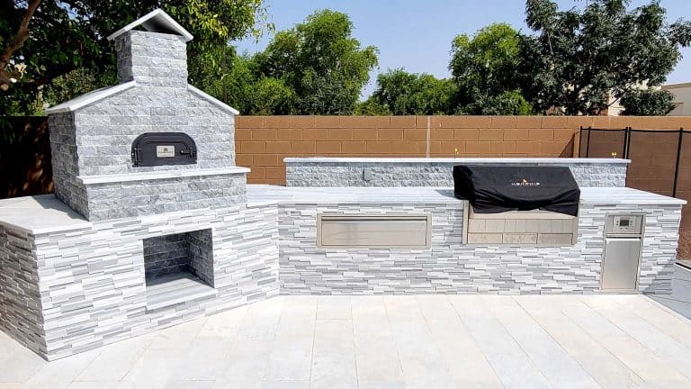 Outdoor kitchen with stone fireplace, grill, and modern design elements.