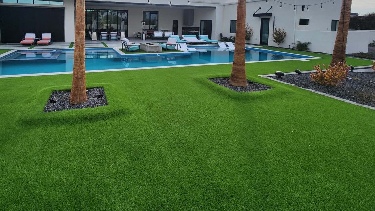 Vivid green artificial turf and a modern swimming pool with lounge chairs, palms, and landscape lighting for a luxurious outdoor space.