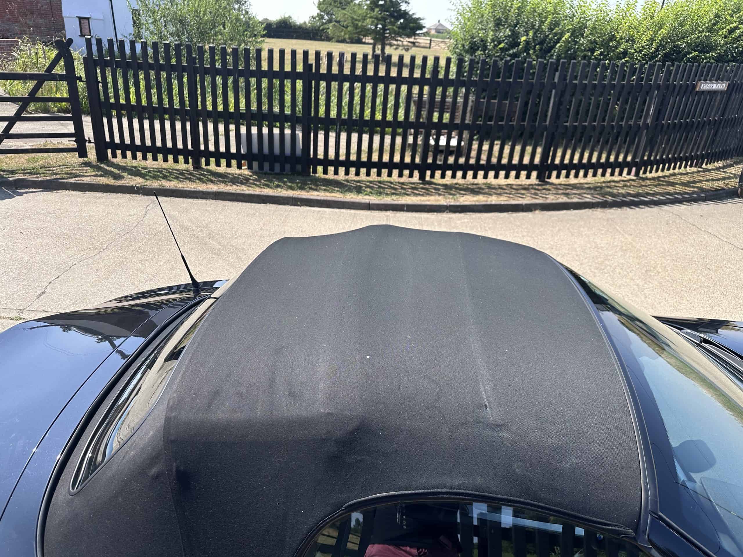 Black BMW Z4 convertible with subtle red features, parked outdoors near a black fence.