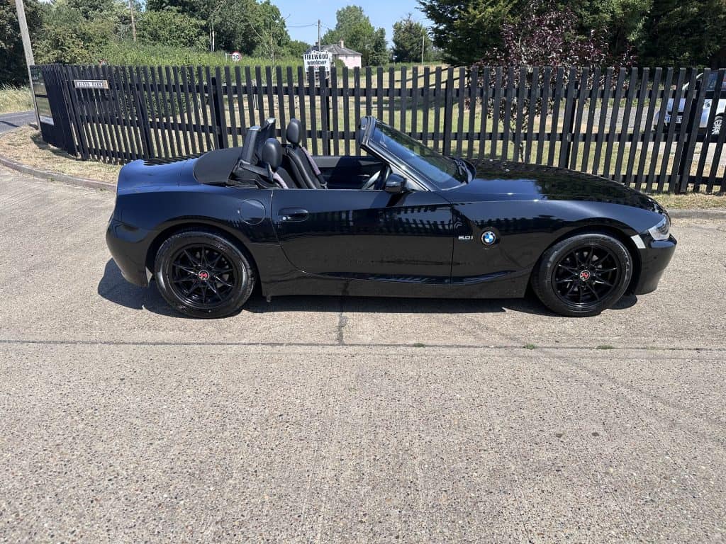 Black BMW Z4 convertible with subtle red features, parked outdoors near a black fence.