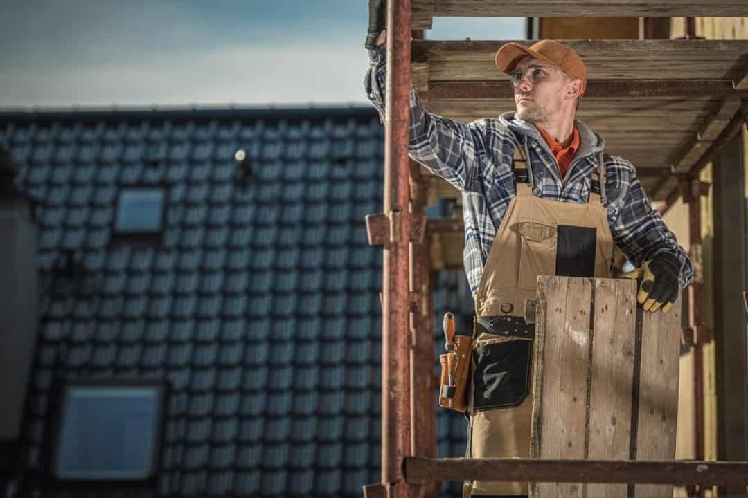 Efficient construction worker inspecting building framework on scaffolding at a residential construction site. Skilled builder ensuring quality and safety during home improvement project.