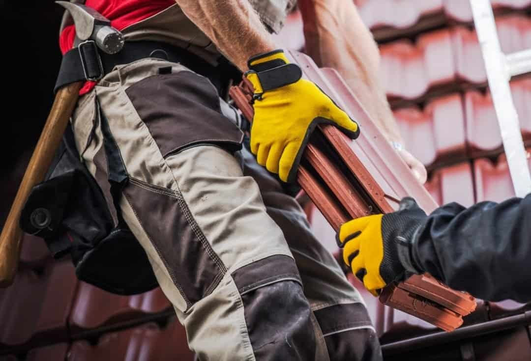 Heavy construction worker wearing yellow gloves installing a roof tile, showcasing expert roofing services offered by Gregorio Soria Construction.