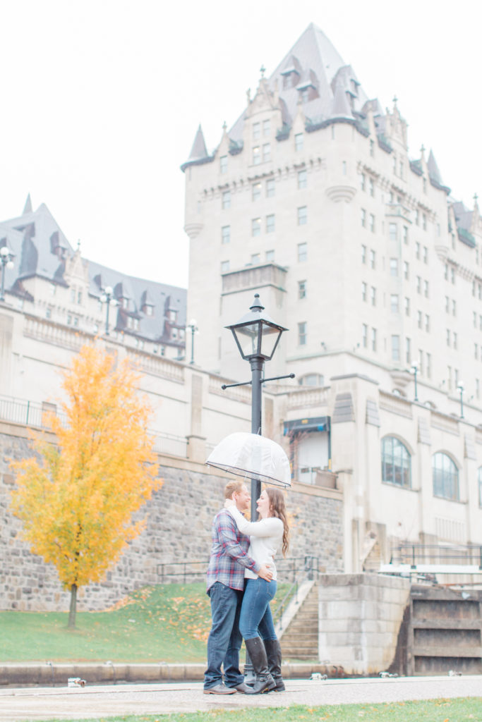 Couple standing in the rain during engagement session with the Locks and Chateau Laurier in the background  - Rainy Day Engagement Session Downtown Ottawa - Photo Locations  Grey Loft Studio - Ottawa Wedding Photographer & Videographer