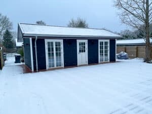 Dark-colored annex building with white doors and trim, surrounded by snow in a winter scene. Screw piles are a great garden room foundation.