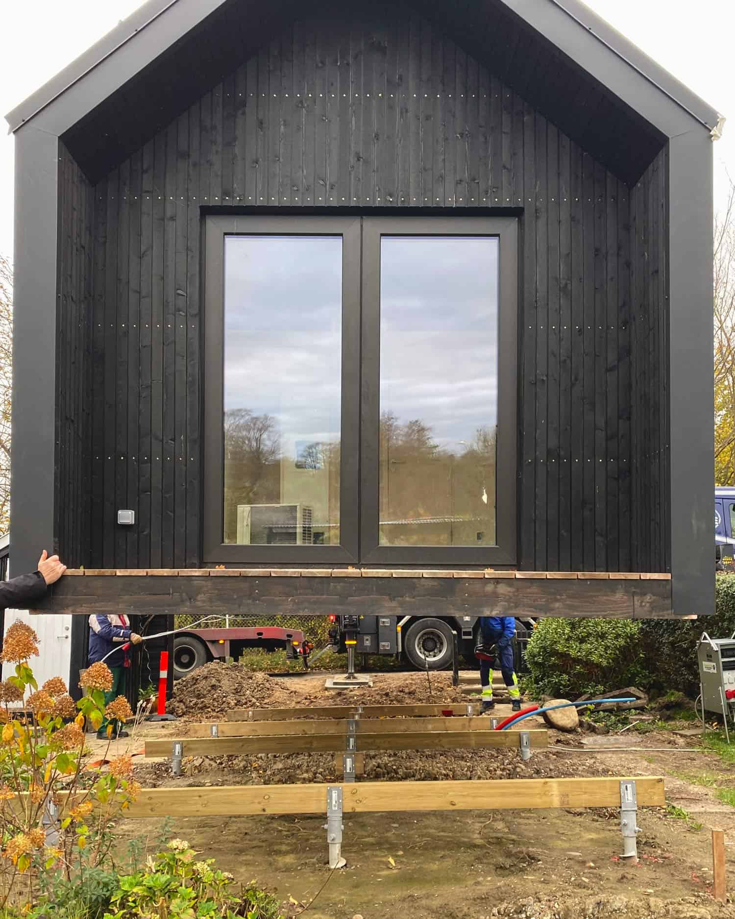 Prefabricated black building section being lowered by crane or machinery onto a prepared foundation with workers guiding it.