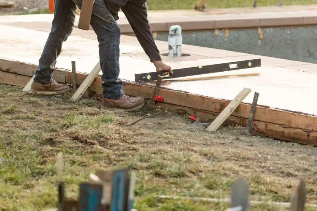 Worker leveling a poured concrete foundation inside wooden forms using a spirit level.