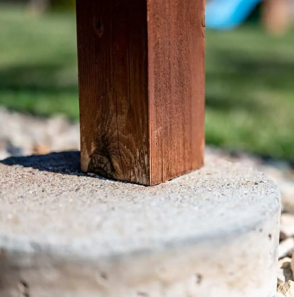 Detail shot showing the base of a wooden deck post supported by a rough concrete footing.