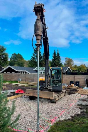 Excavator with a drilling attachment installing a ground screw foundation at a construction site.