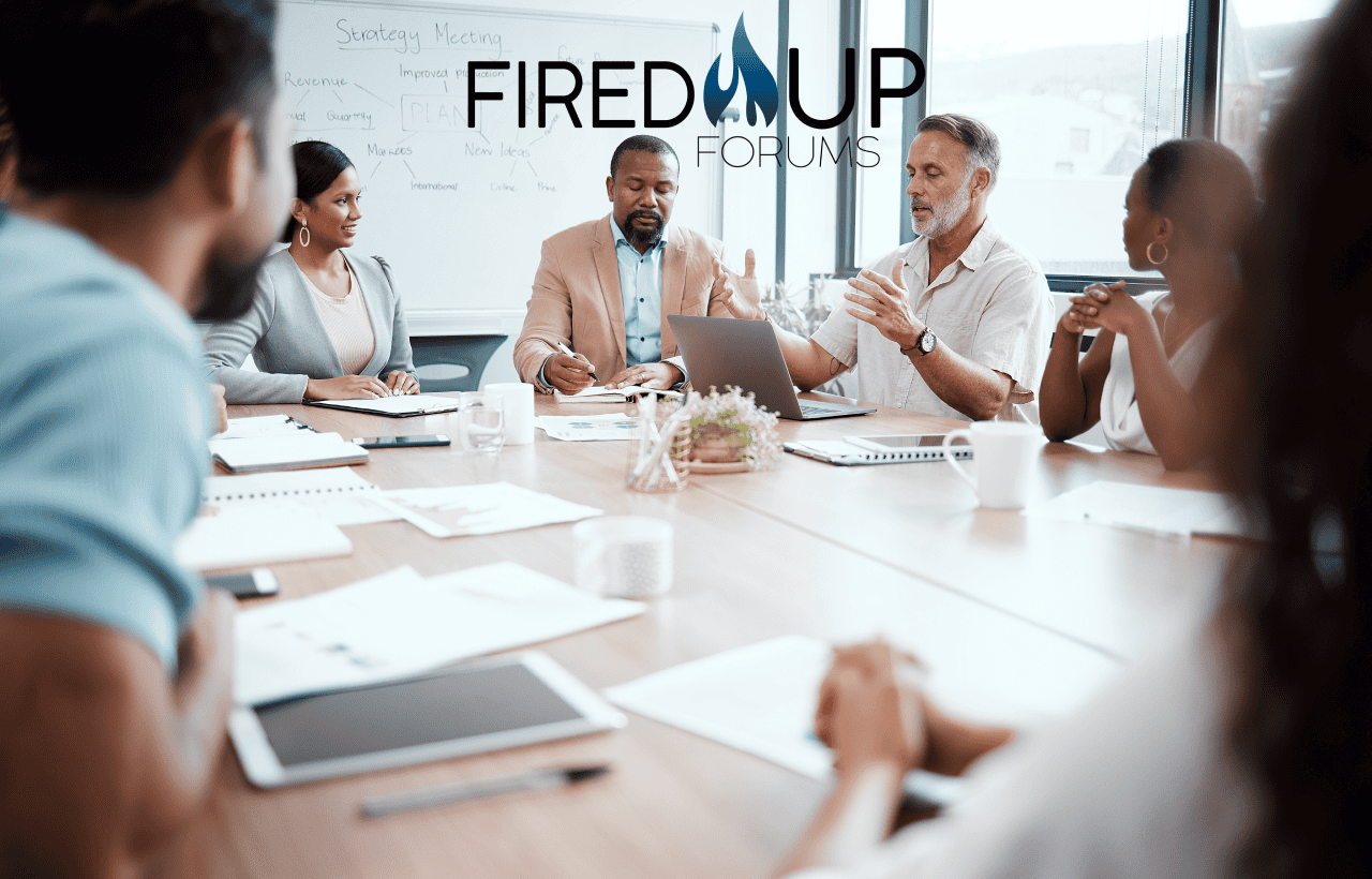 Fired Up Forums team engaged in a strategy meeting, discussing plans and ideas around a conference table with notes and laptops