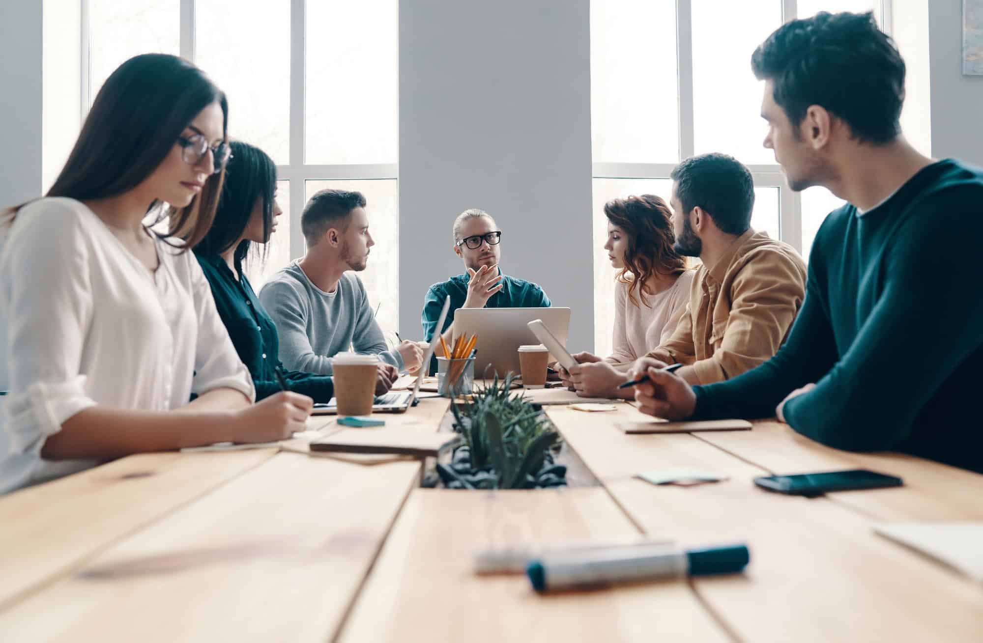 Team of young professionals engaged in a meeting around a long wooden table in a bright modern office