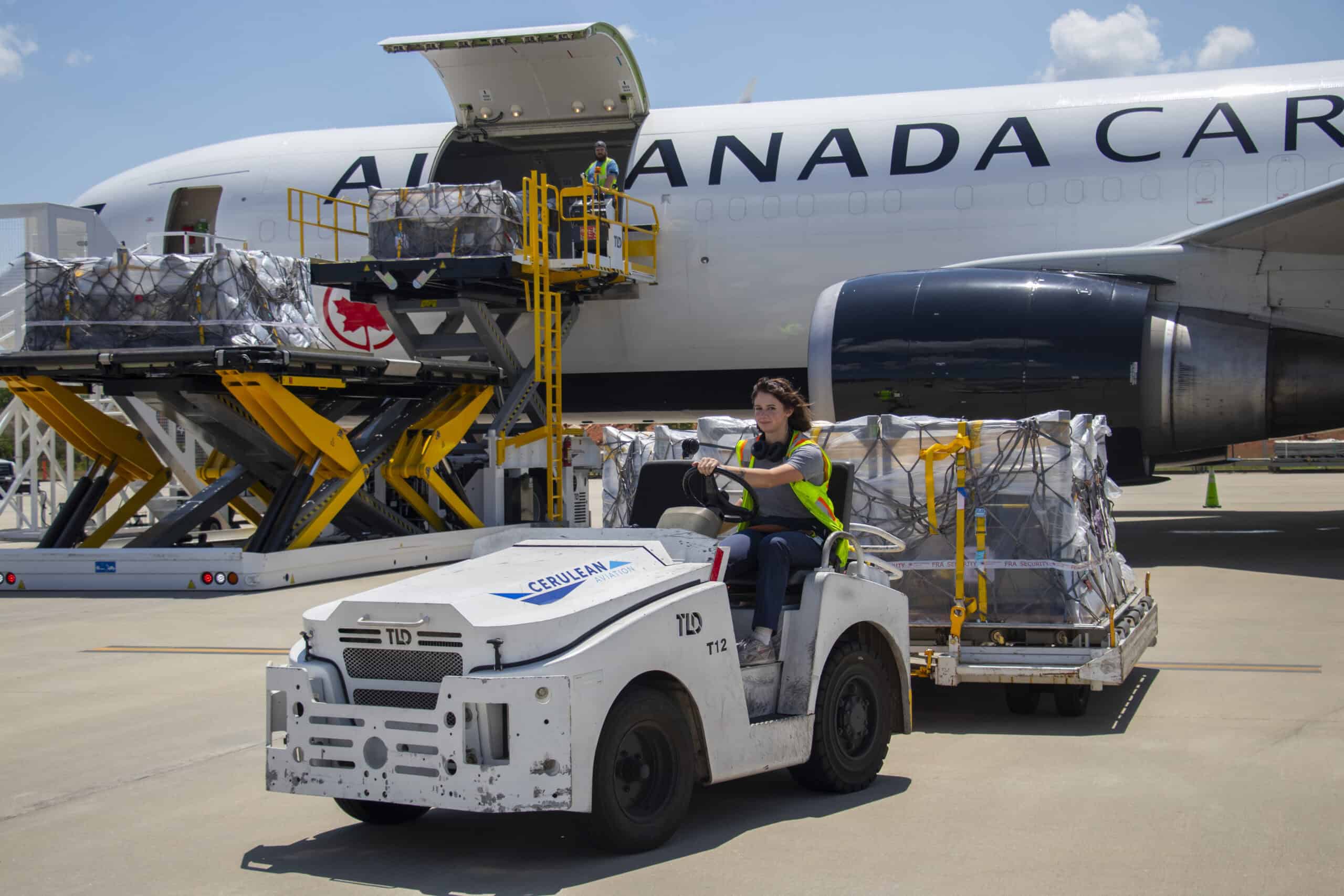 Image of Cerulean Aviation Cargo employee on a cargo tug in front of an Air Canada plane.