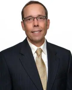 Professional headshot of Kent Bontrager wearing a dark pinstripe suit, white dress shirt, and a patterned gold tie, posed against a neutral background.