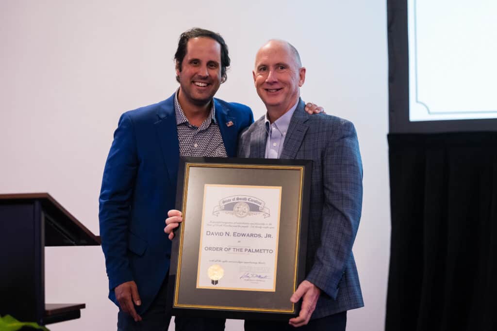South Carolina Senator Josh Kimbrell stands beside Greenville-Spartanburg International Airport President and CEO Dave Edwards. Both are smiling as they hold a large framed Order of the Palmetto certificate presented to Edwards
