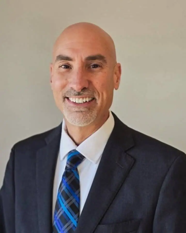 Professional headshot of GSP Chief of Police William Petty smiling at the camera, wearing a dark suit jacket, white dress shirt, and blue patterned tie against a light neutral background.