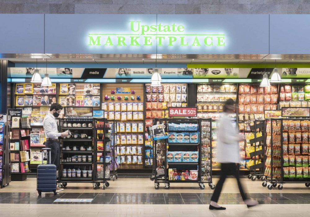 Upstate Marketplace facade with man looking at souvenirs and woman walking in front of store.